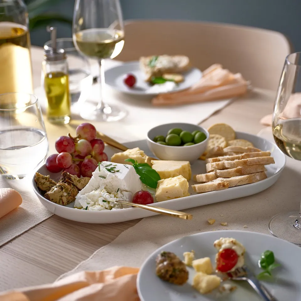 White porcelain dish, holding cheese, grapes, olives & crackers. Smaller than a wine glass, placed near it.