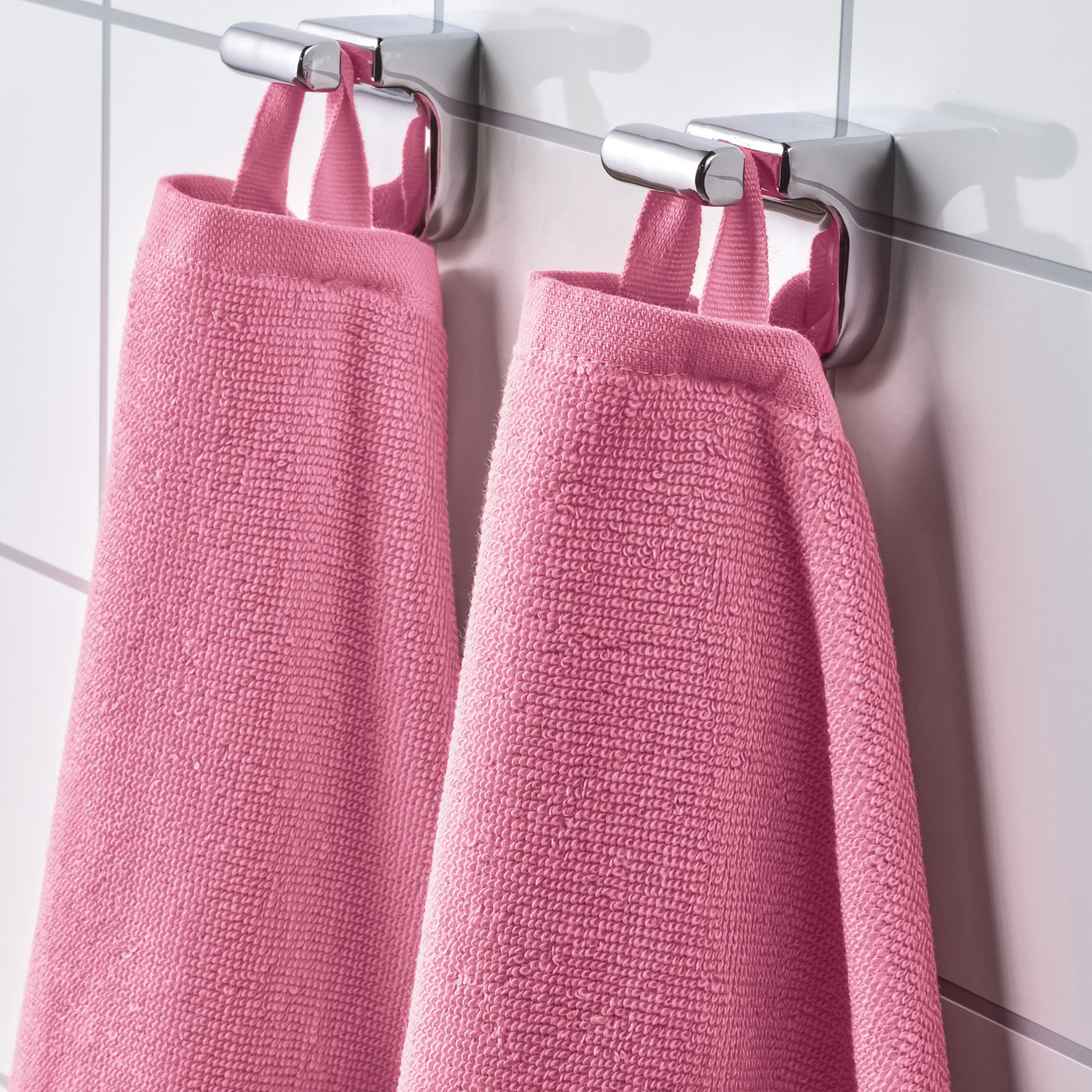 Two pink towels hang side by side on metal hooks, showcasing their absorbent and soft terry texture.