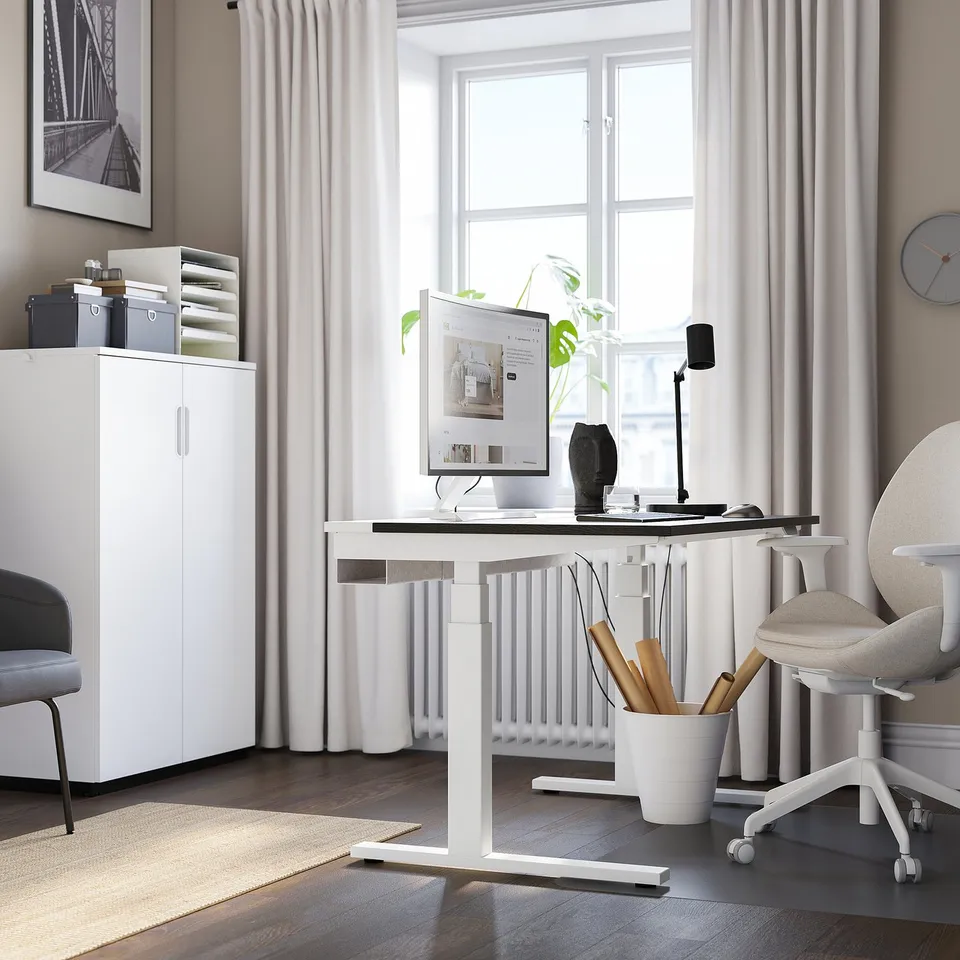 Home office: white MITTZON sit/stand desk, chair, white cabinet, large window, plant, computer.