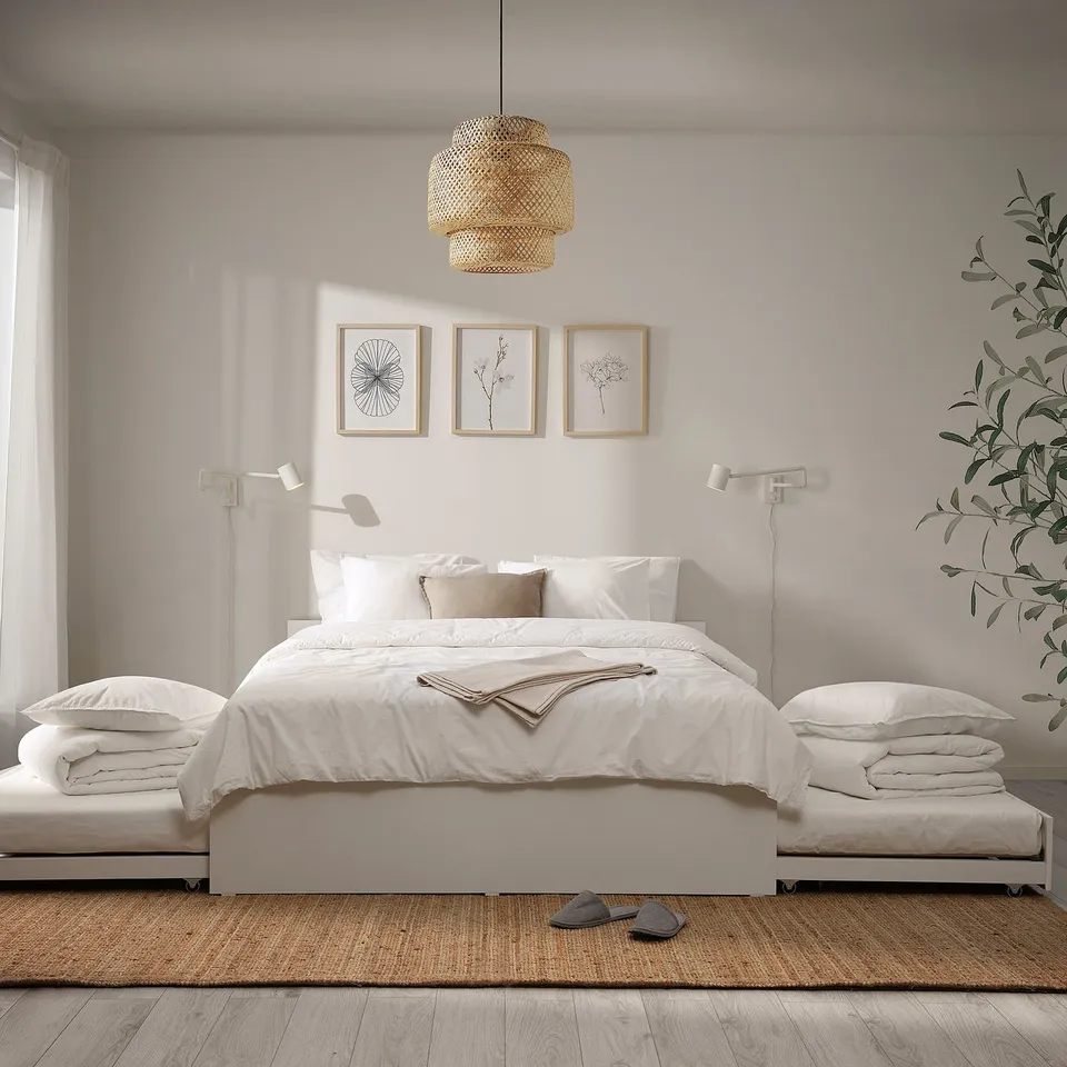 Modern bedroom with white VIHALS bed, two trundles, clean lines, pendant light, botanical prints, and wall lamps. Jute rug and large plant.