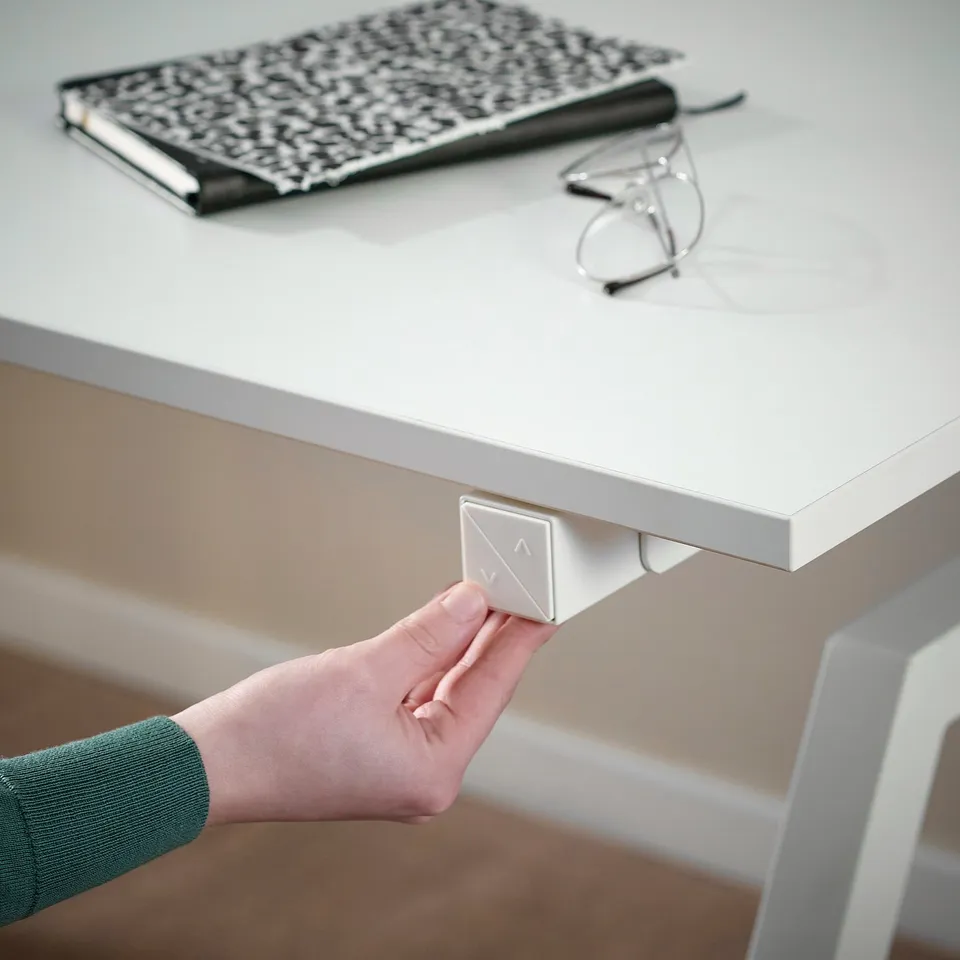 Person adjusting TROTTEN sit/stand desk, featuring single motor lift, ensuring flexibility and comfort.