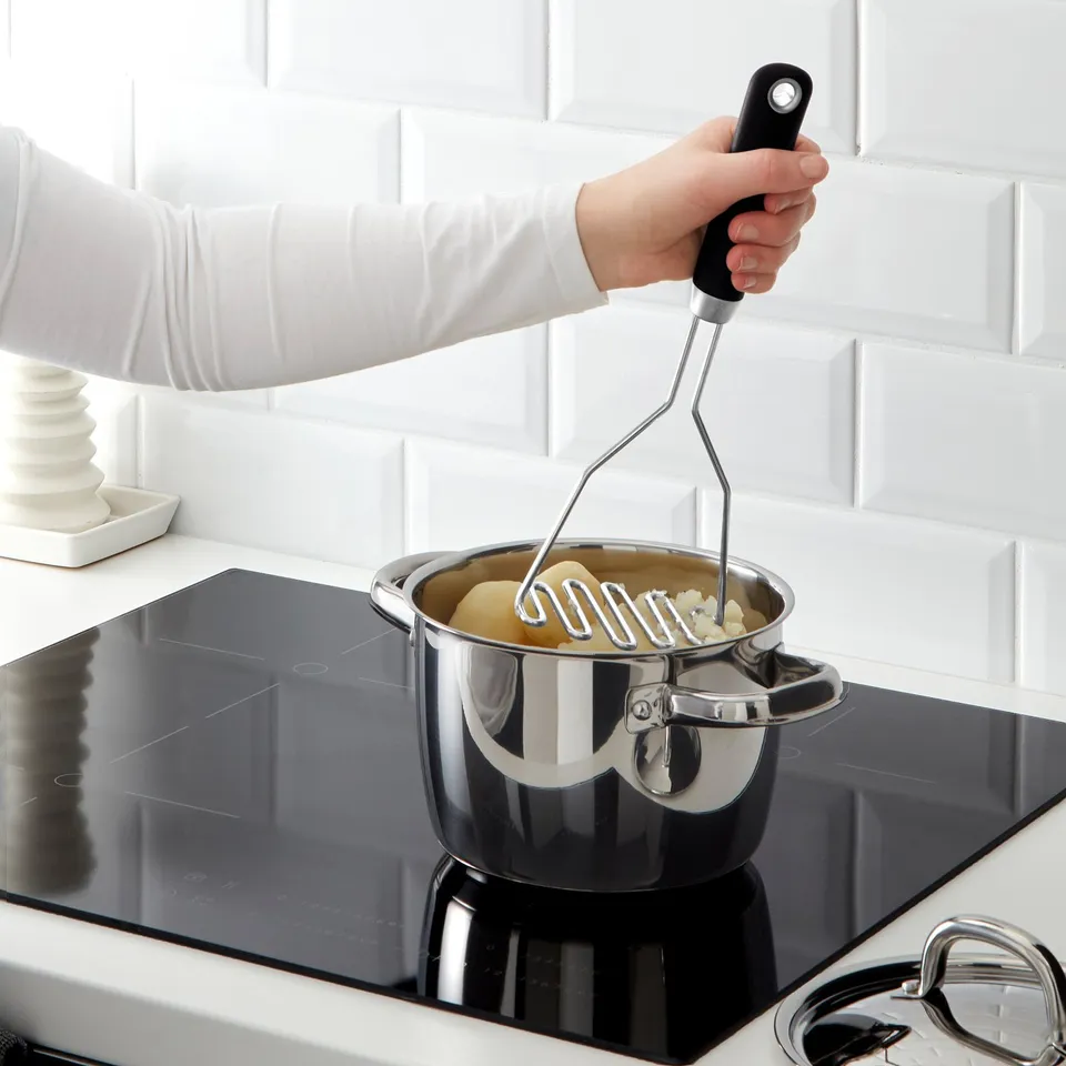 Person uses IKEA potato masher on stovetop, demonstrating its firm grip and functional design.