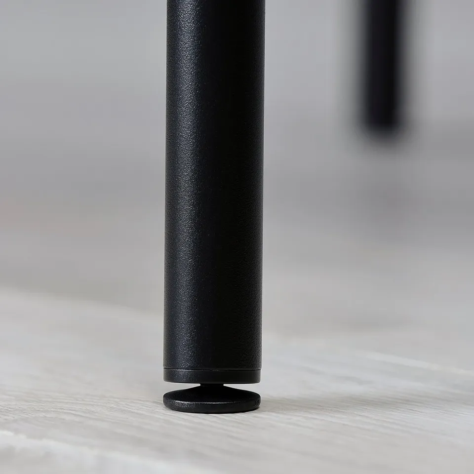 Black table leg with smooth, textured surface and round base, standing on light-colored tabletop.
