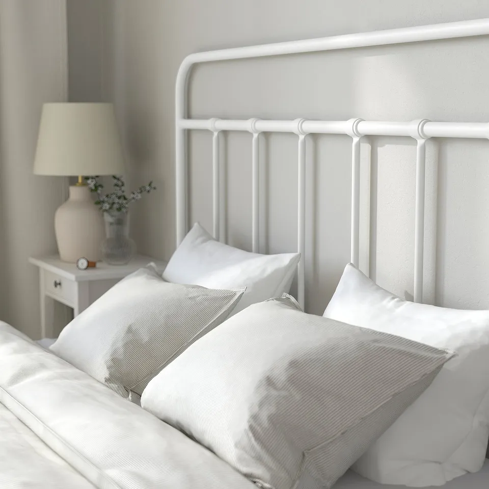 White metal bed frame with curved headboard, holding white pillows and blankets, showcasing a cosy and clean bedroom setup.