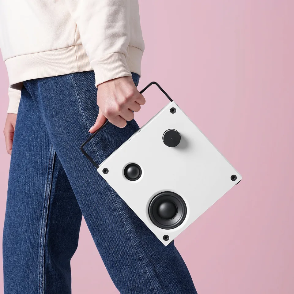 A person holds a white VAPPEBY bluetooth speaker, showcasing its handle and speakers.