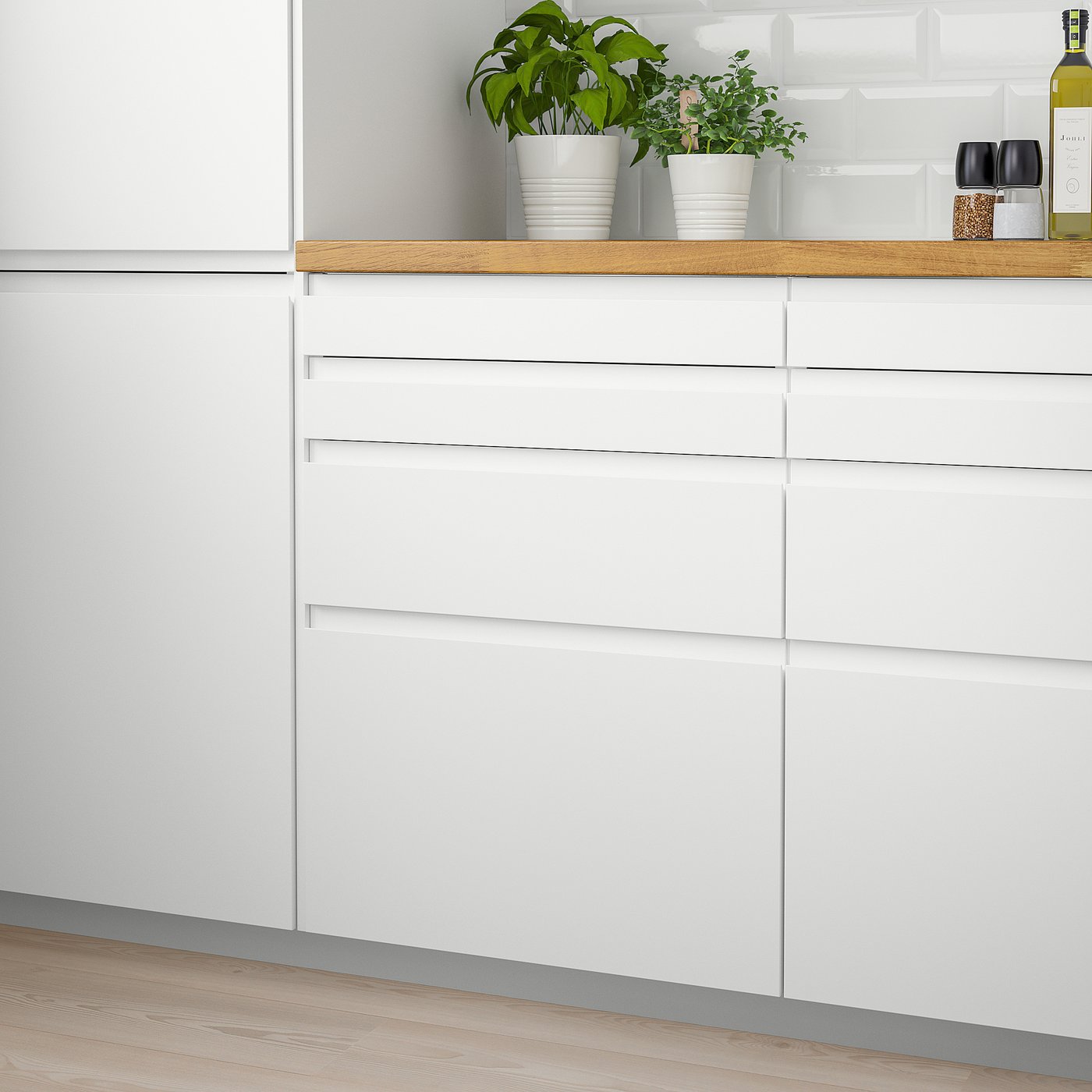 Modern kitchen with matte white VOXTORP drawers and potted plants on top.