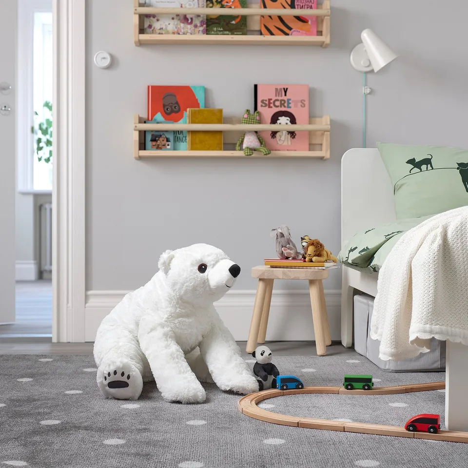 Large white polar bear cuddly toy sits next to a train track, surrounded by childrens toys and books in a cosy bedroom.