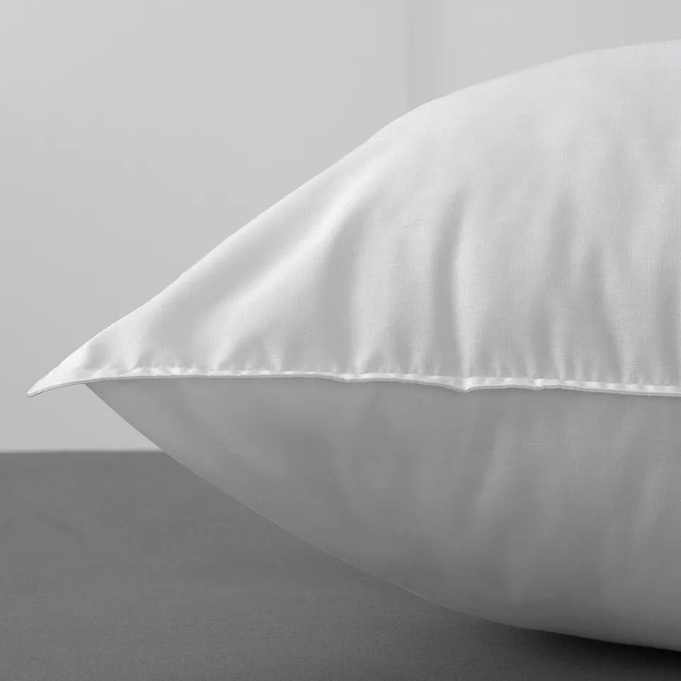 A close-up of a white pillow with even stitching on a light background.