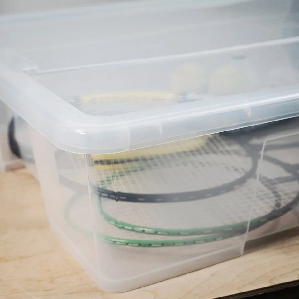 Clear plastic storage box with lid, containing two tennis rackets, showcasing durability and transparency.