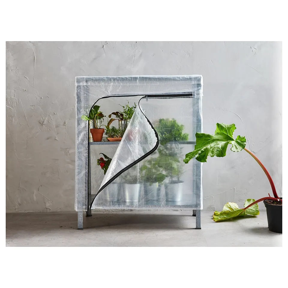 The HYLLIS greenhouse cover, a clear plastic enclosure for a shelving unit, housing various green plants.