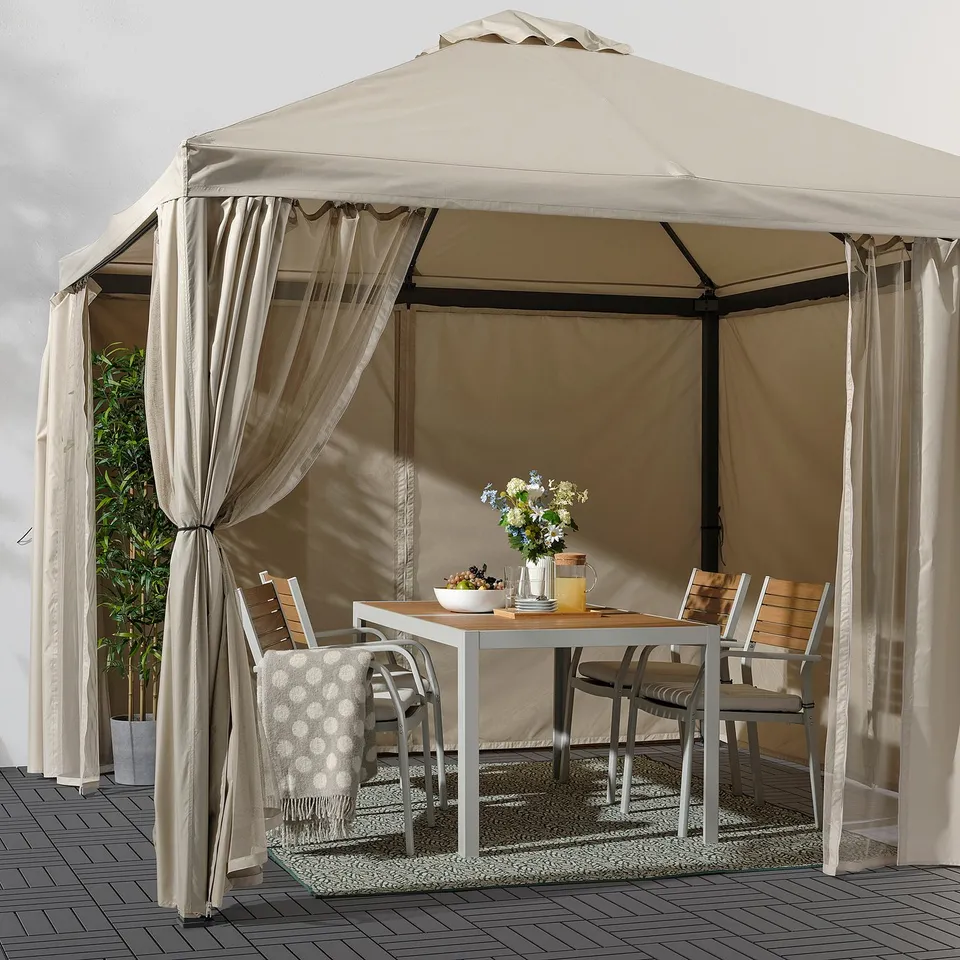 HIMMELSÖ beige gazebo offers shaded outdoor dining with a table, chairs, and curtains.