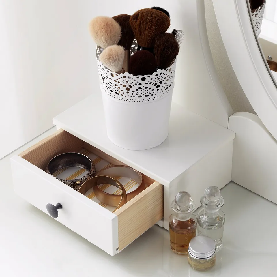 A dressing table with open drawers and a container of makeup brushes.