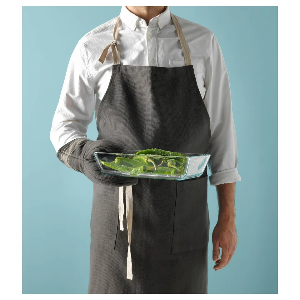 Person wearing black apron holding glass tray with green vegetables.