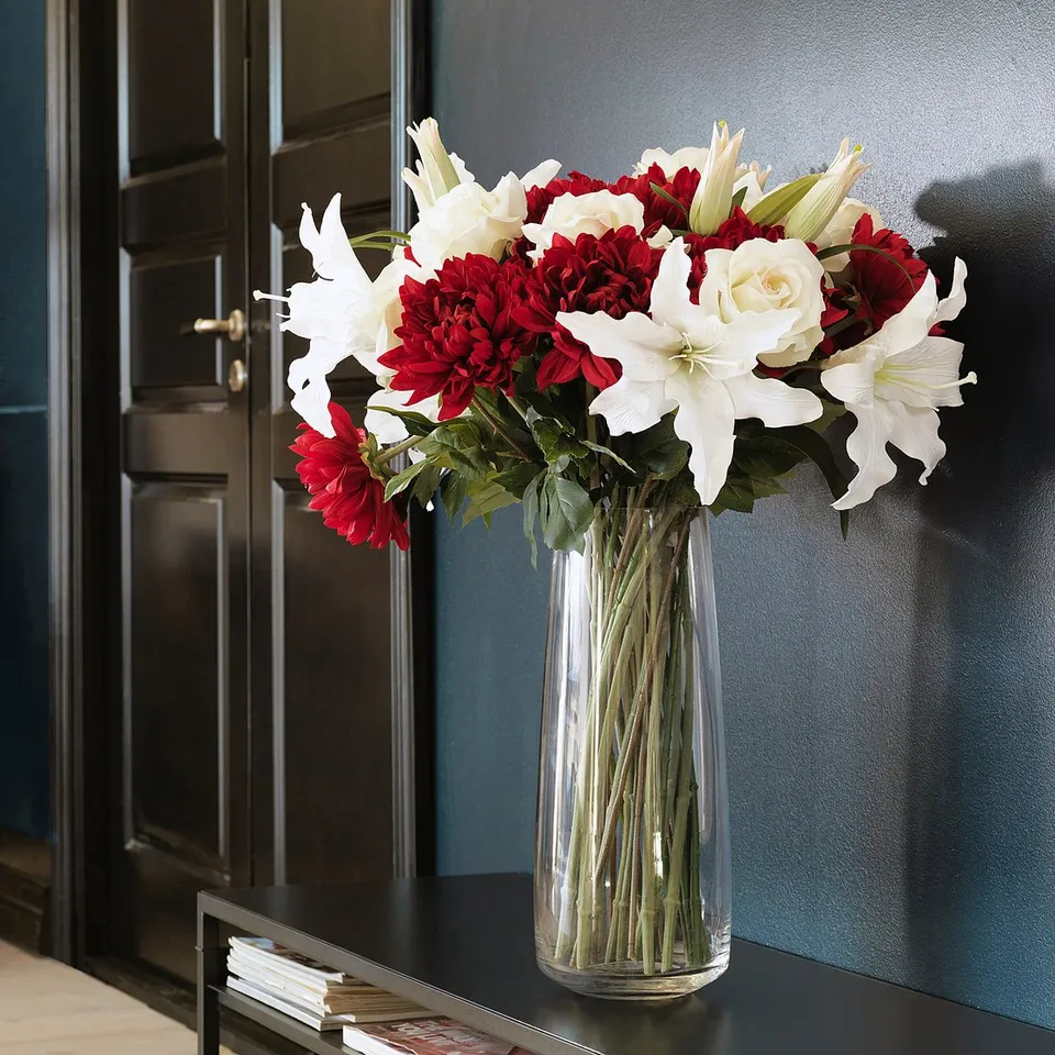 Vase with white lilies and red flowers on dark table. Modern, elegant interior.