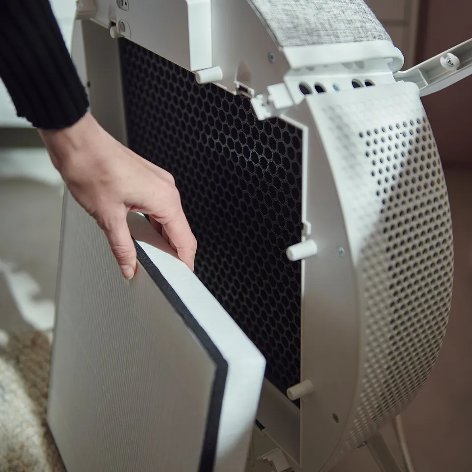 Person holding white STARKVIND air purifier with mesh and philtres, adjusting settings.