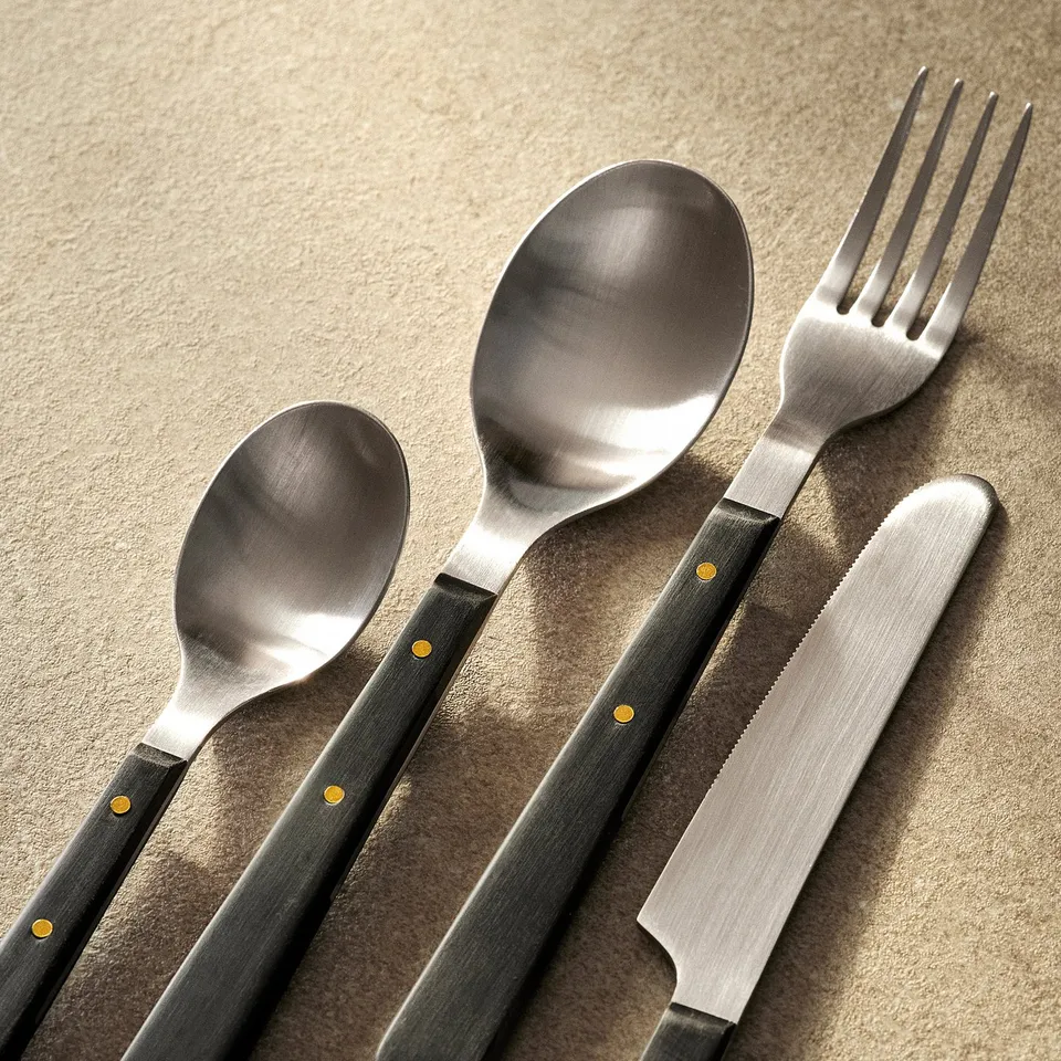 Polished stainless steel cutlery with matte finish and gold accents, arranged neatly on a textured surface.