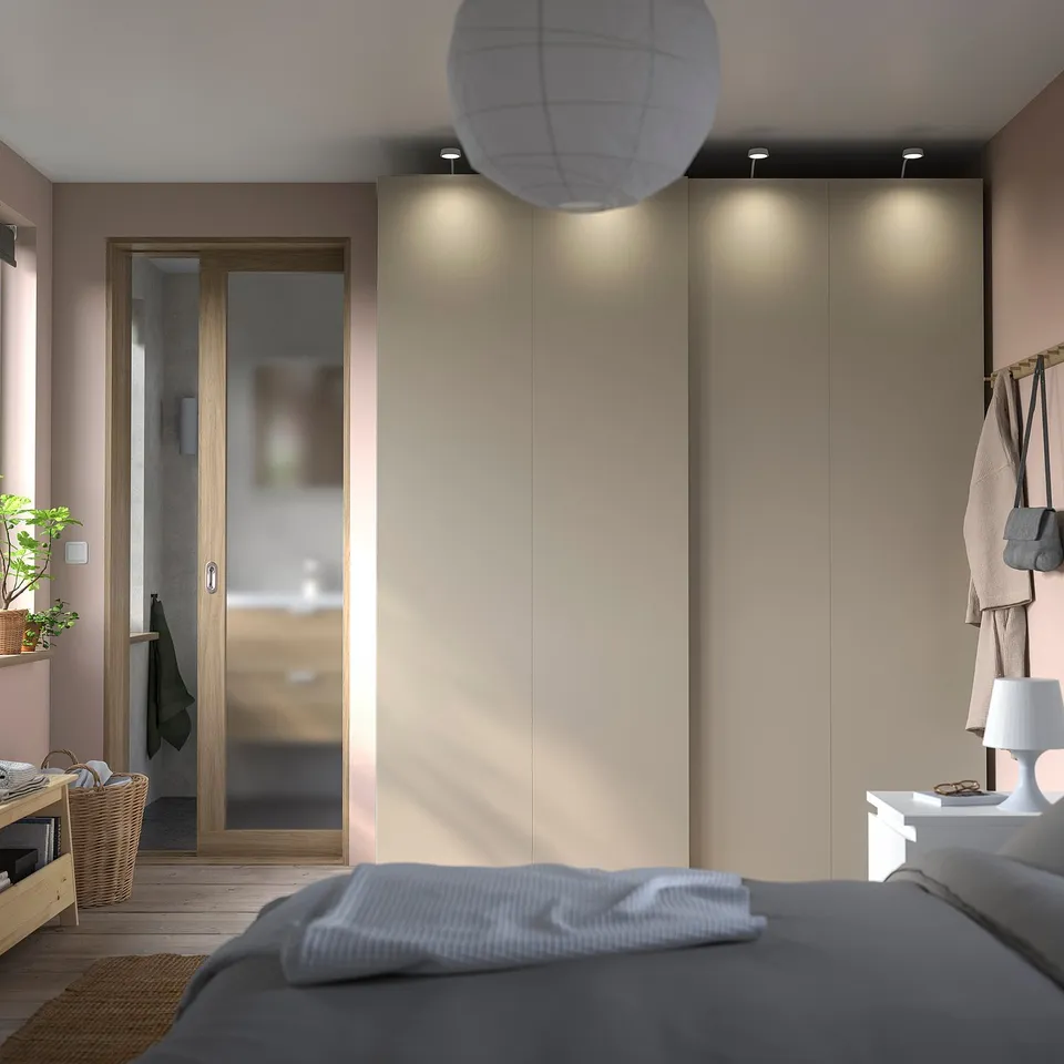 Modern bedroom featuring HASVIK sliding doors with soft-close mechanism, light wood finish, grey bedding, and hanging coats.