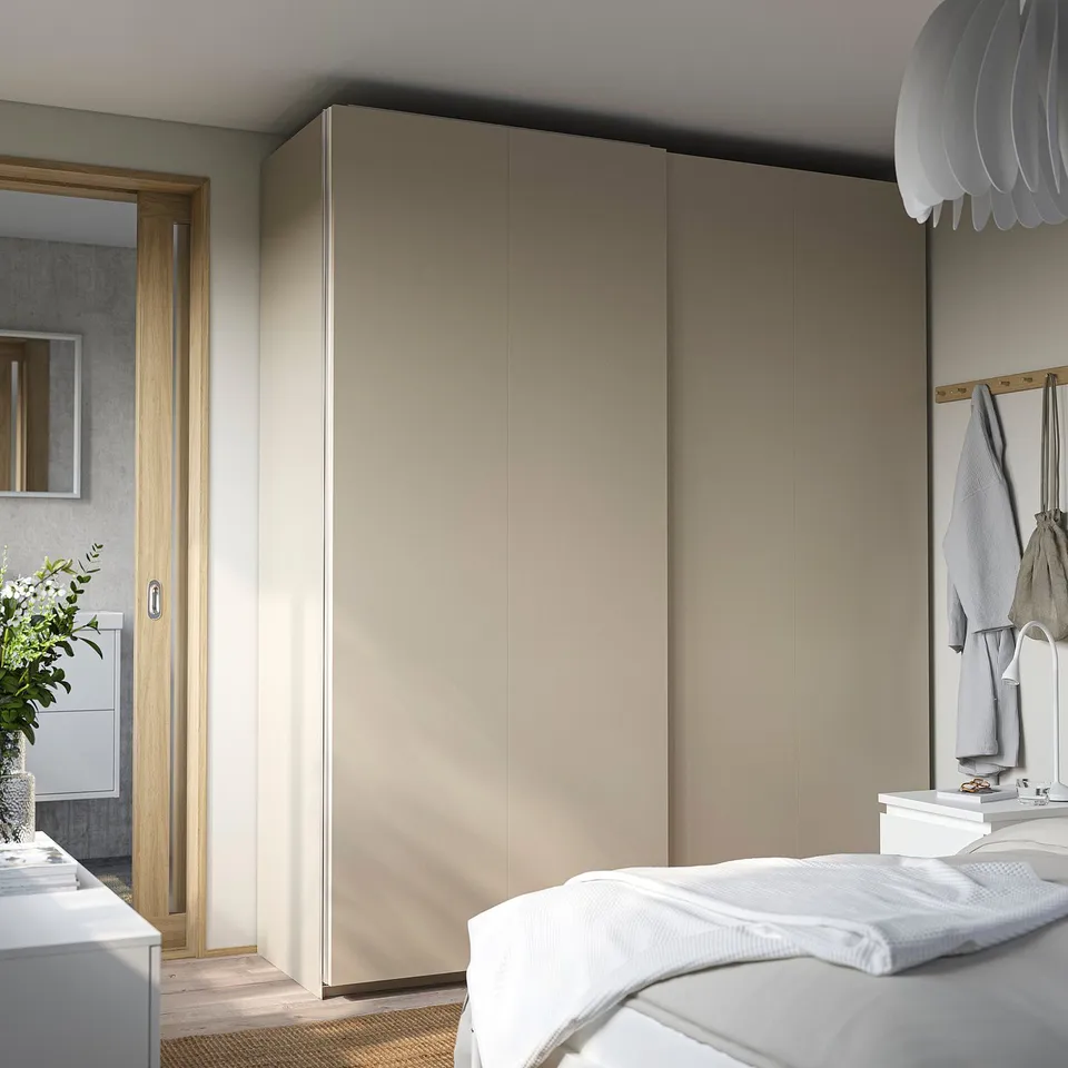 Modern beige PAX wardrobe with sliding doors fills bedroom wall, taller than white bed.