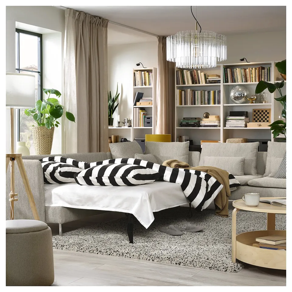 Grey sofa-bed, bookshelves, striped pillows, table with cup, books, rug.