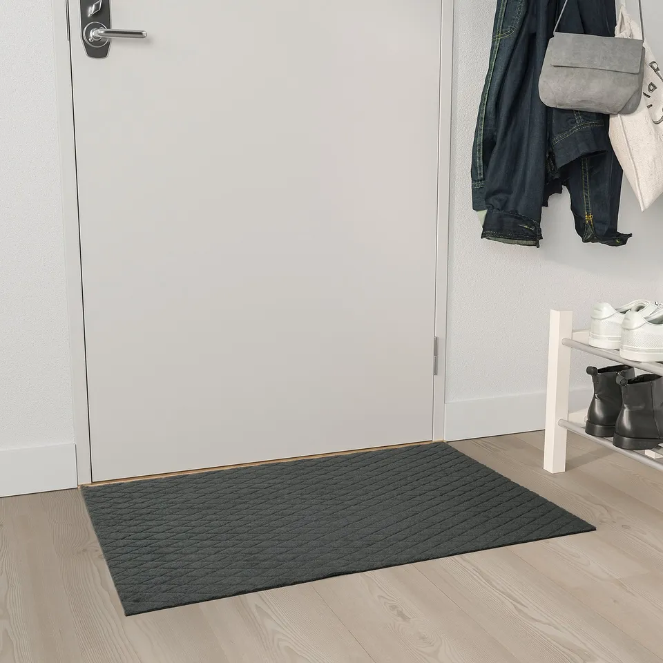 Grey ÖSTERILD mat near white door, recycled polyester, textured.