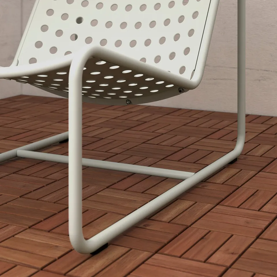 Close-up of a modern white metal chair with perforated seat and back on wooden deck.