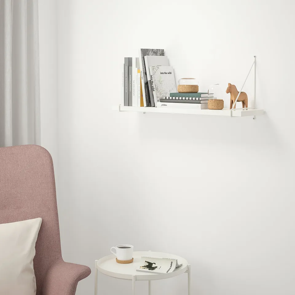 White BERGSHULT wall shelf with books, above red chair with white cushion. Small table holds coffee cup and magazine. Fits well above chair.