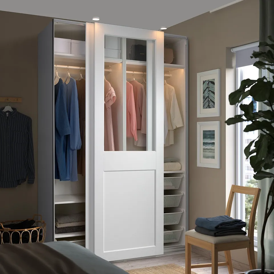 White PAX wardrobe with glass doors, displaying clothes and accessories in a bright room.
