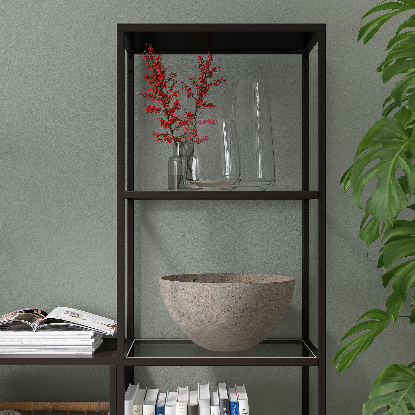 Modern black bookshelf with glass shelves, displaying books, decor, vases, and a stone bowl.