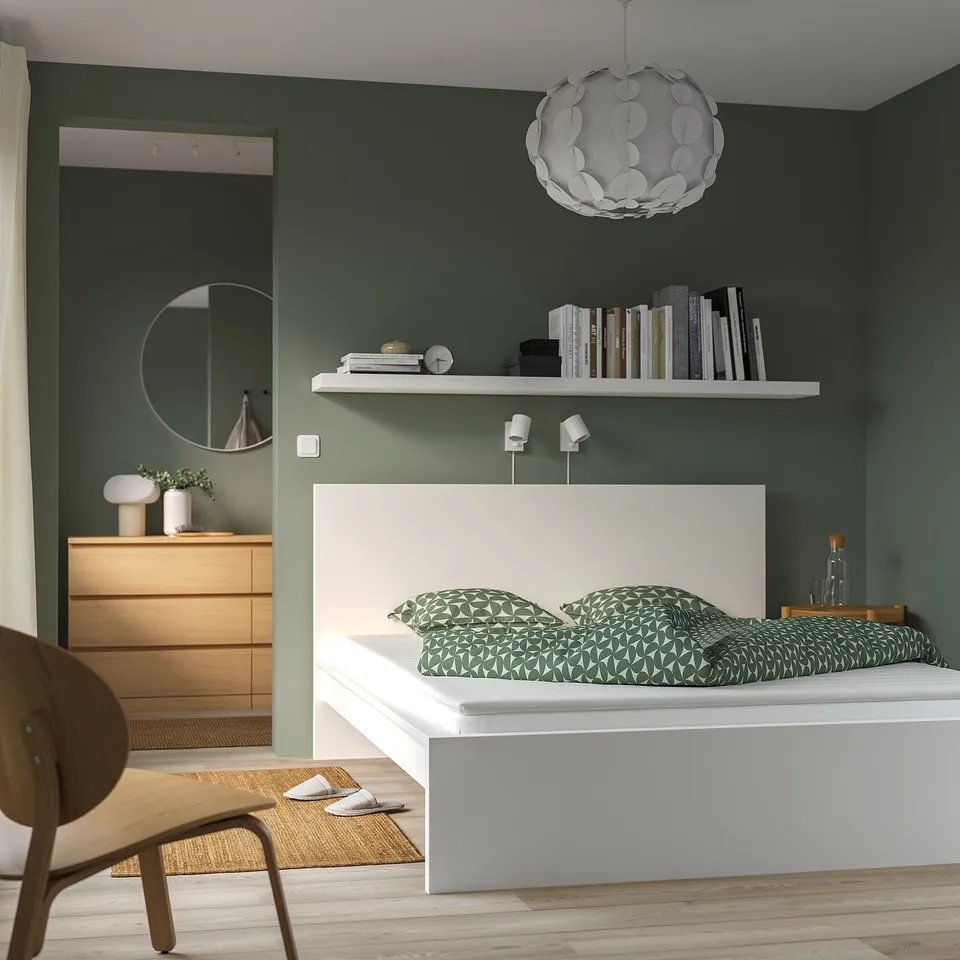 Modern bedroom: green wall, white bed, shelf, lamp, dresser, mirror, chair, slippers.