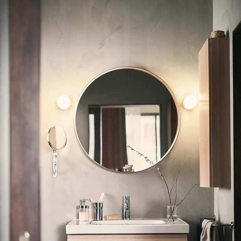Modern bathroom with floating light wood vanity, round mirror, chrome fixtures, and black and white tiled floor.