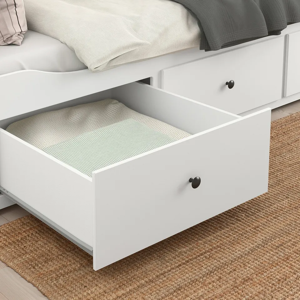 White HEMNES daybed with drawers open, showing storage space and black knobs, on jute rug.