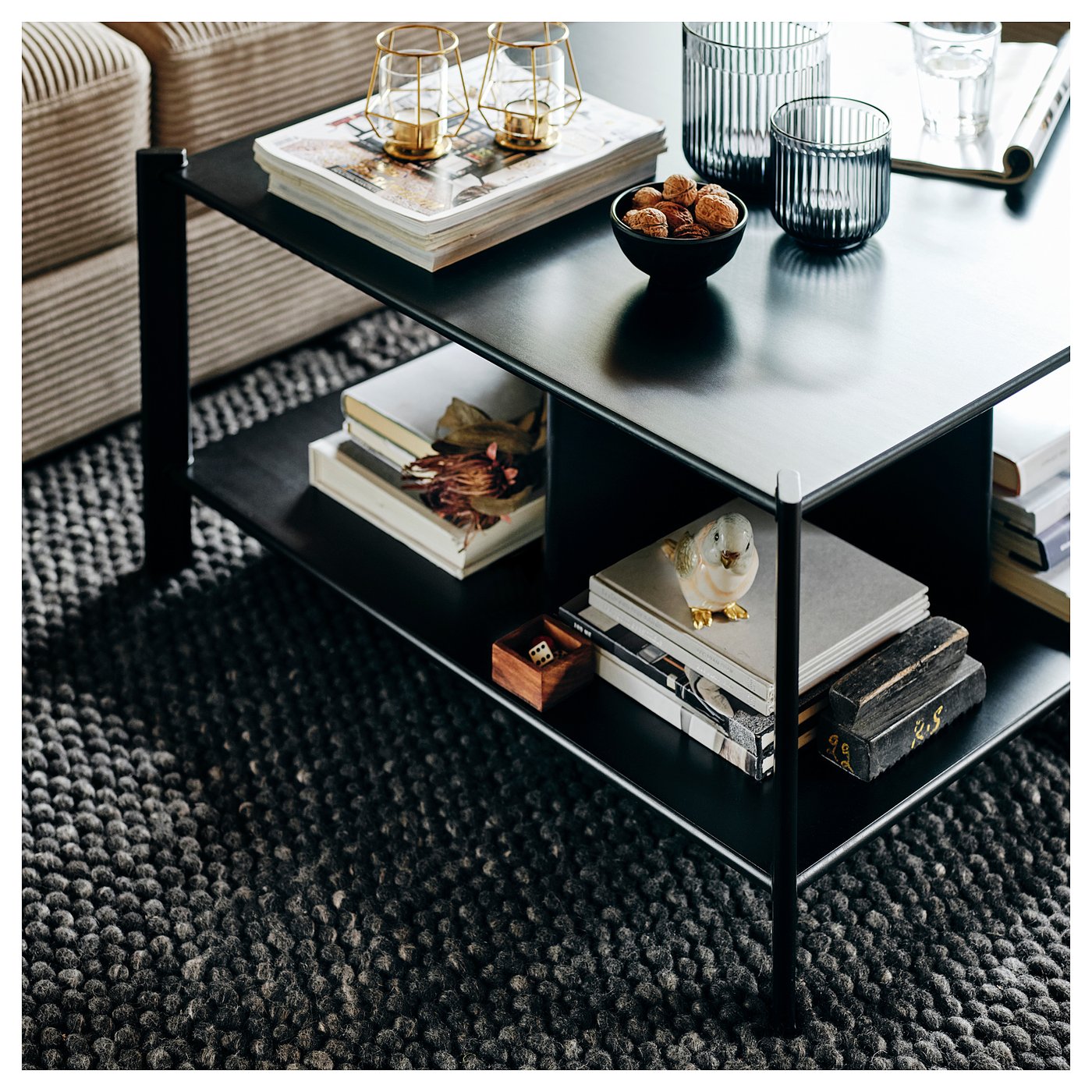 Black coffee table with bamboo shelves, metal legs, books, and decor items.