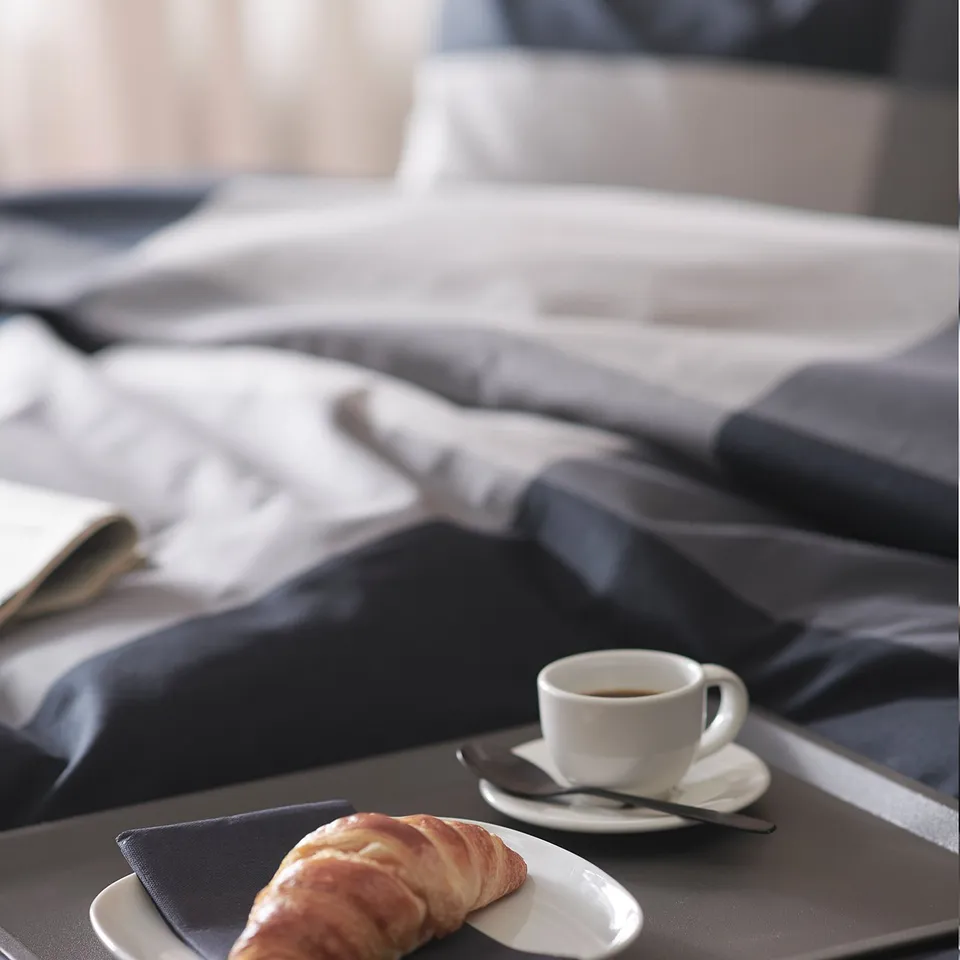 Black tray with white coffee cup and pastry on bed.