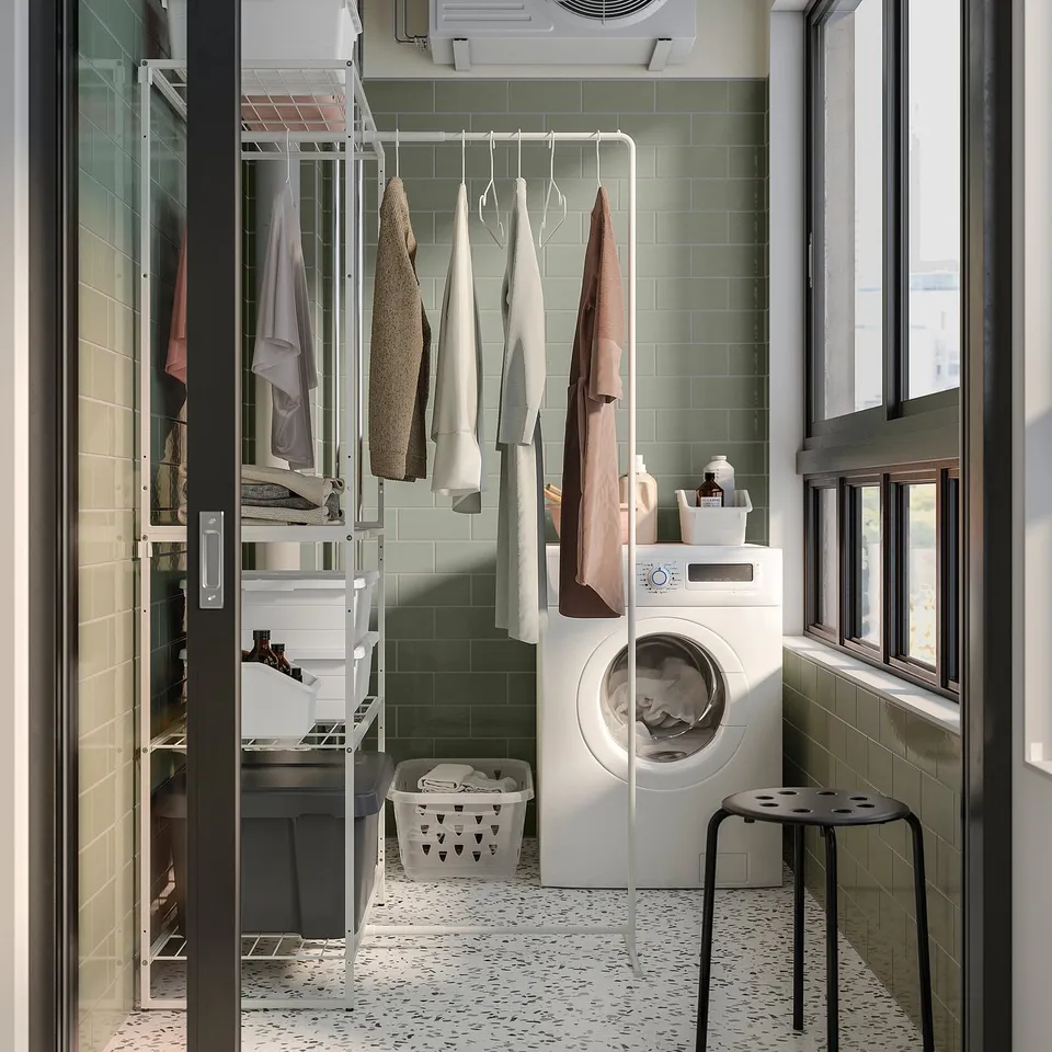 Small laundry room with green tiles, white JOSTEIN storage unit, drying rack, washing machine, and stool.