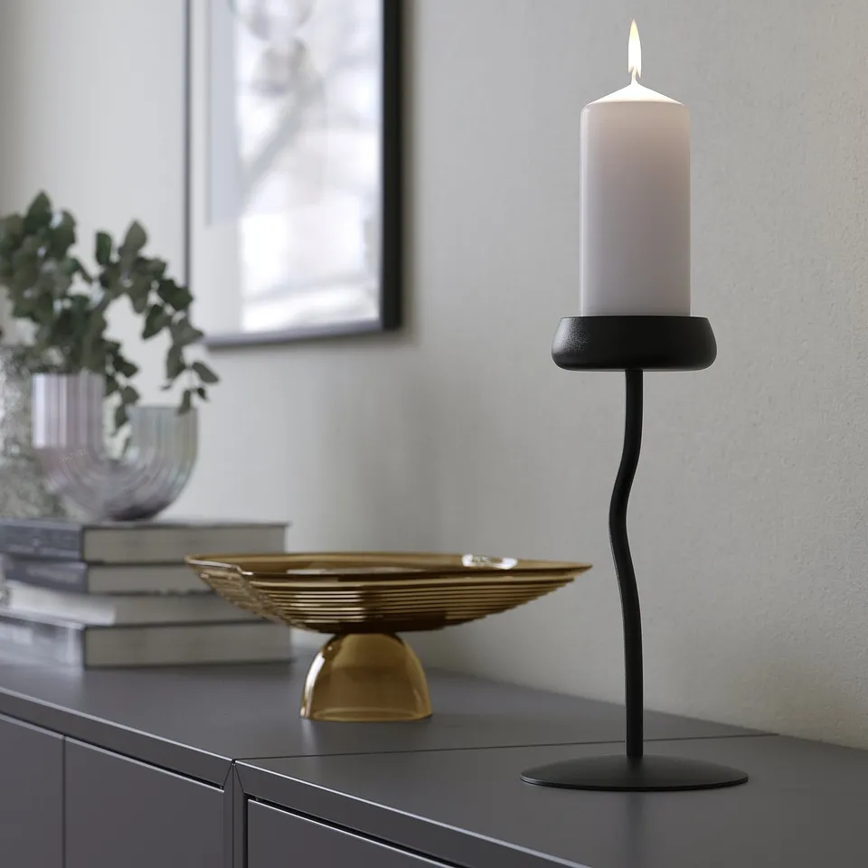 Modern black candle holder with white pillar candle, stylishly curved, on dark cabinet.
