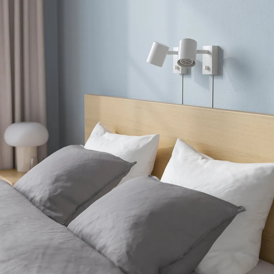 A bed with a wooden headboard, pillows, and a wall-mounted adjustable lamp.