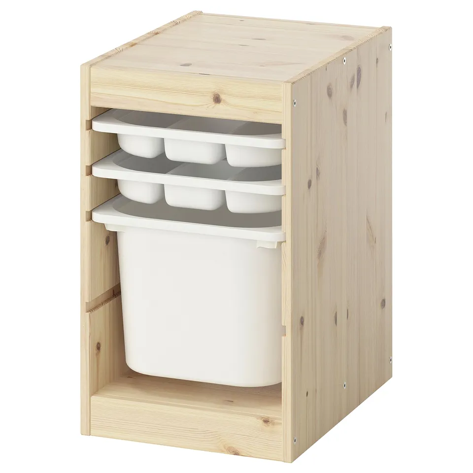 Depicts a TROFAST storage unit; light wood, with open compartments and white plastic trays and bin.