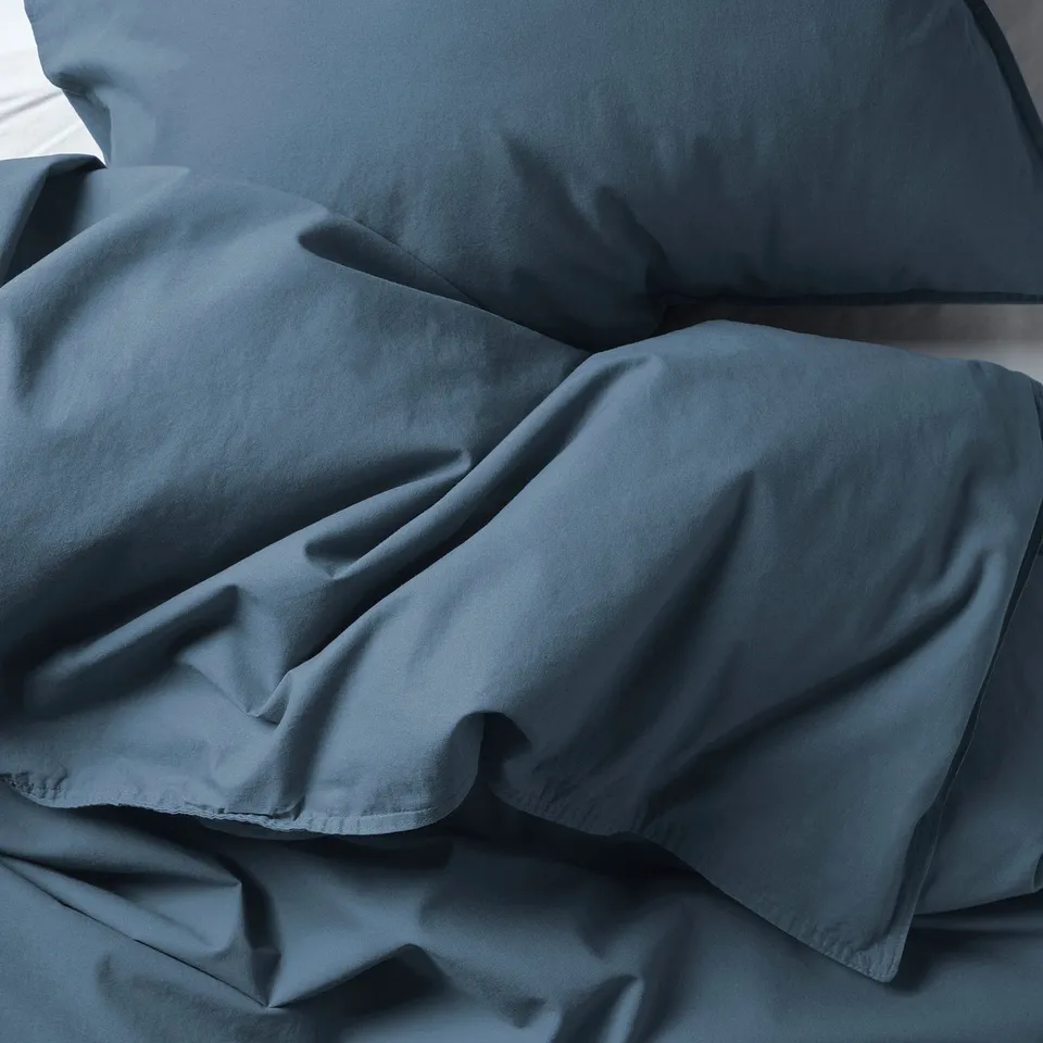 A neatly made bed with a smooth, deep blue duvet cover, suggesting high-quality, soft, and comfortable cotton material.