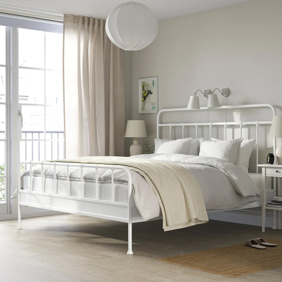Minimalist bedroom with white metal bed, curved headboard, and neutral bedding. Durable powder-coated steel, pendant lamp, and bedside table.