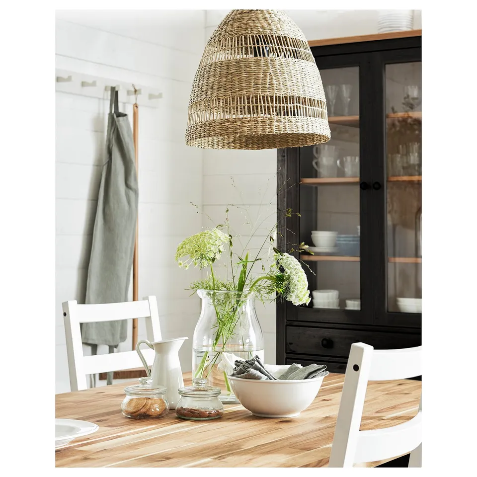 Wicker pendant lamp TORARED above wooden table, warm glow.