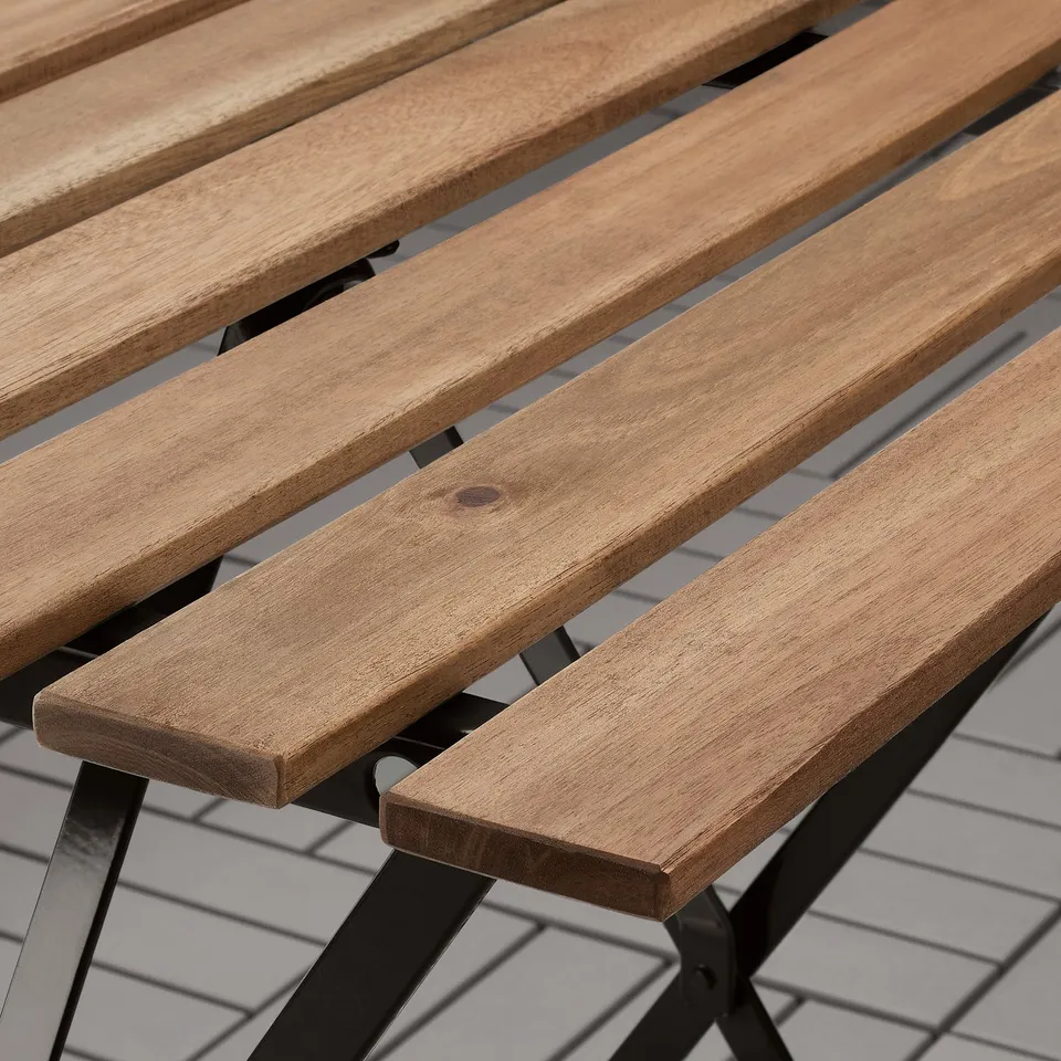 Wooden patio table with black metal legs, displaying natural wood grain and sturdy construction.