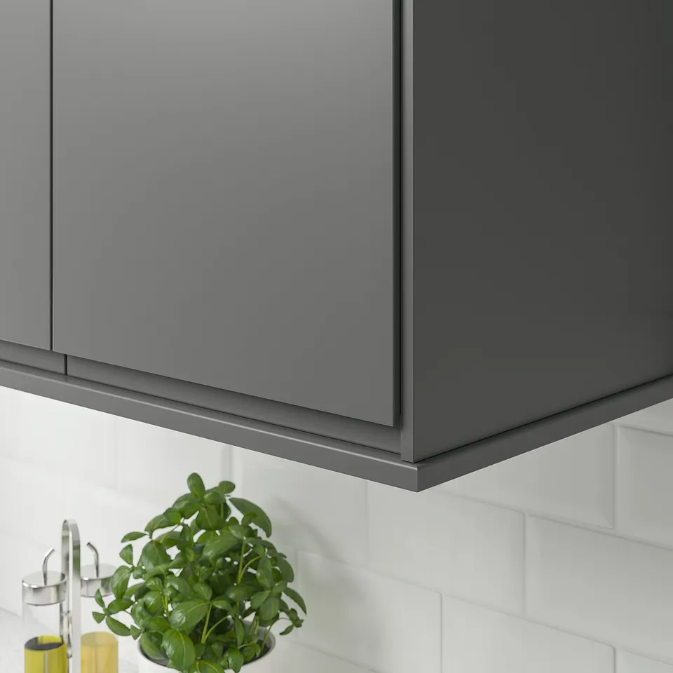 Grey kitchen cabinet trim, hiding cords, with plant and utensils.