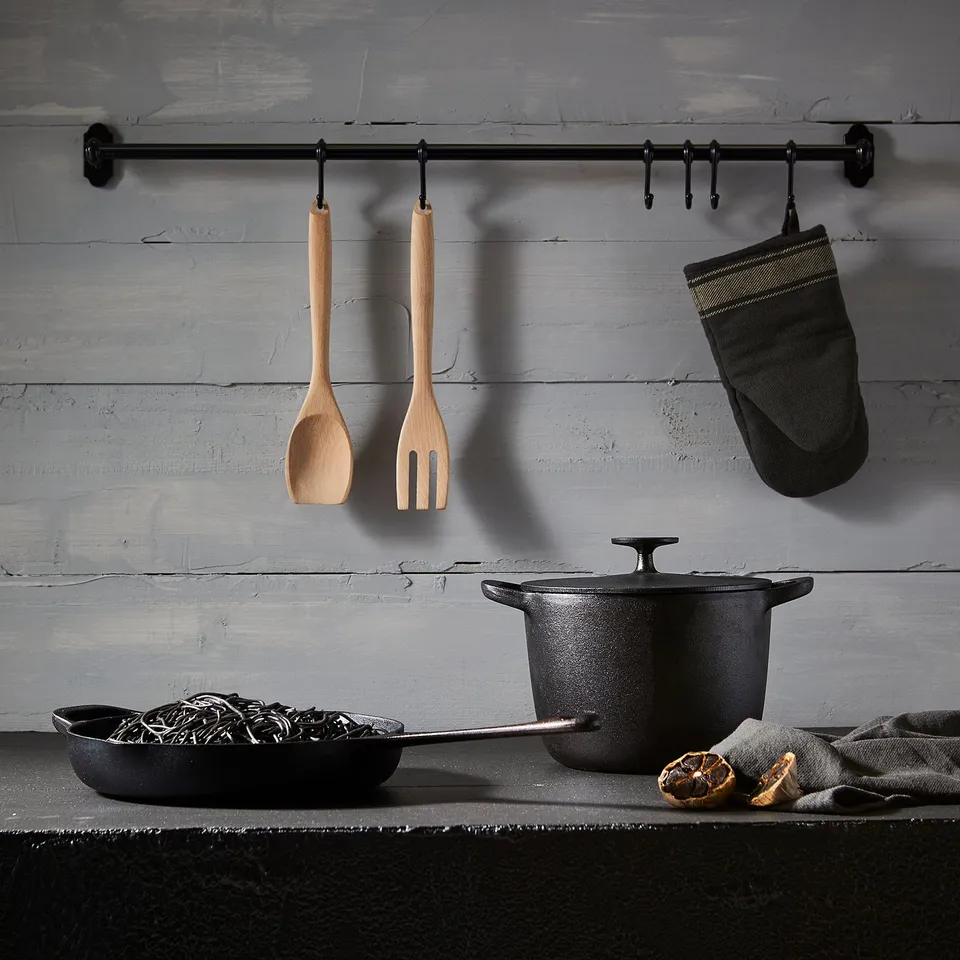 Wooden utensils, black cookware, oven mitt, citrus, grey cloth, weathered wall hooks