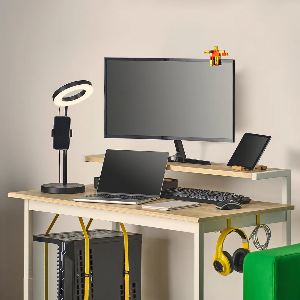 A compact gaming setup with a height-adjustable desk, monitor shelf, cable management, and hanging headphones.