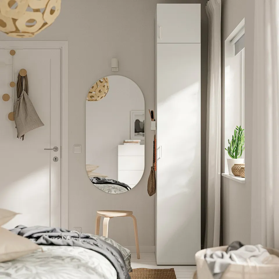 Modern bedroom with large LASTARE wardrobe, mirror, stool, and plant. Neutral bedding, coat hooks, light curtains.