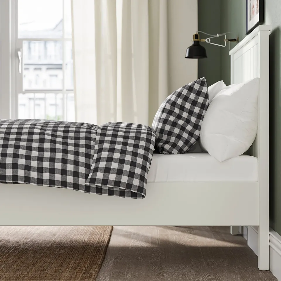 Bed with black and white chequered bedding, two pillows, white headboard, and lamp.