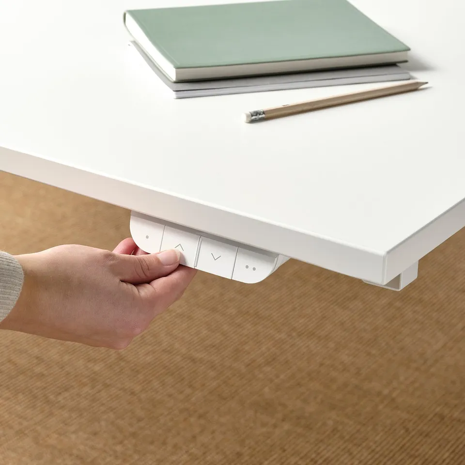 Person adjusting controls on electric sit-stand desk, altering height with two memory settings.
