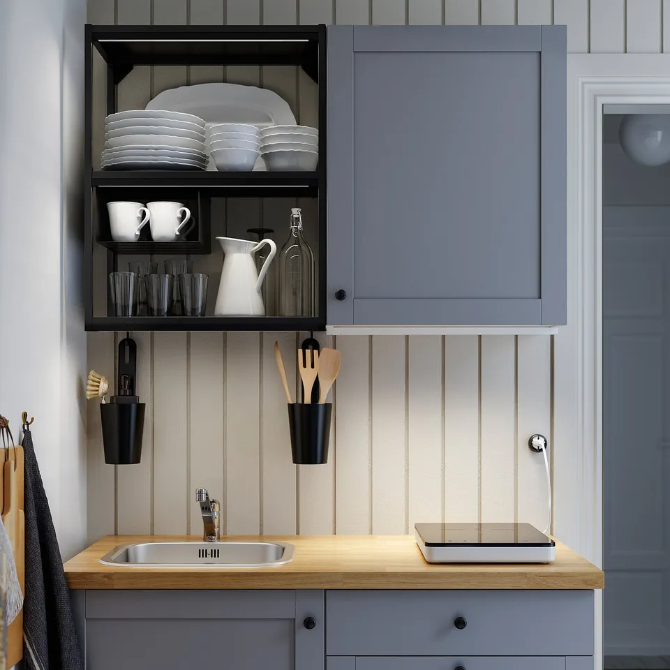 Kitchen with grey SKYDRAG cabinet, plates on black open shelf, sink and counter space with wooden utensils and soap dispenser.