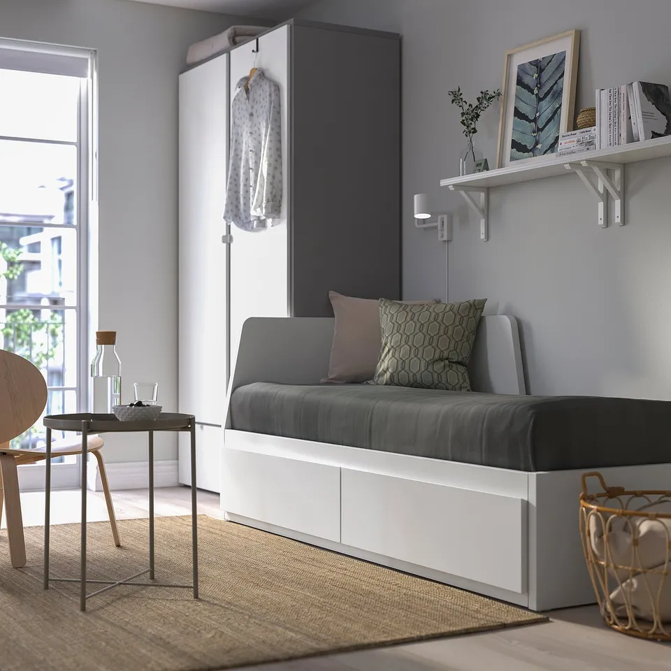 Grey FLEKKE sofa-bed near window, minimalist with storage, transforms into bed.