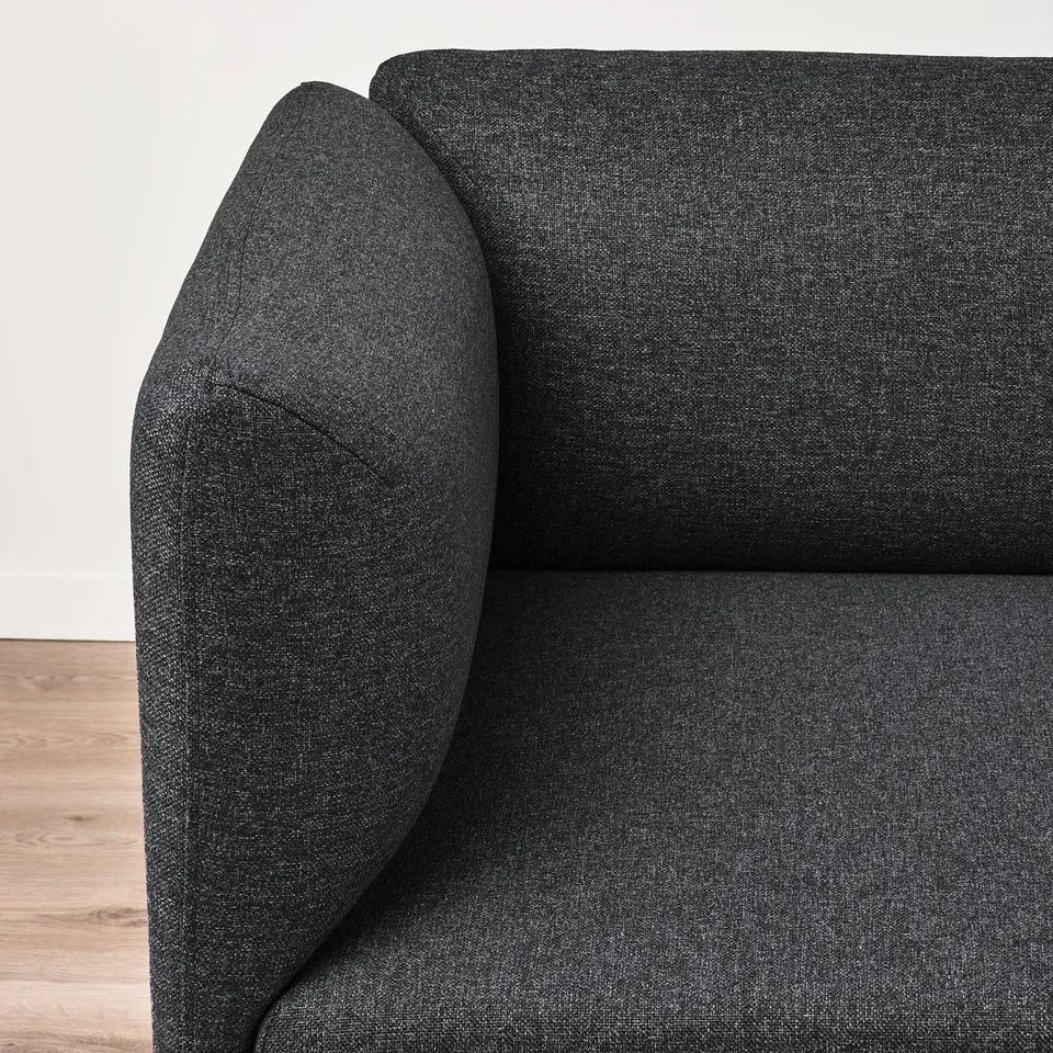 Dark grey sofa corner with plush, rounded arms on wooden floor, showcasing its cosy, high-quality design.